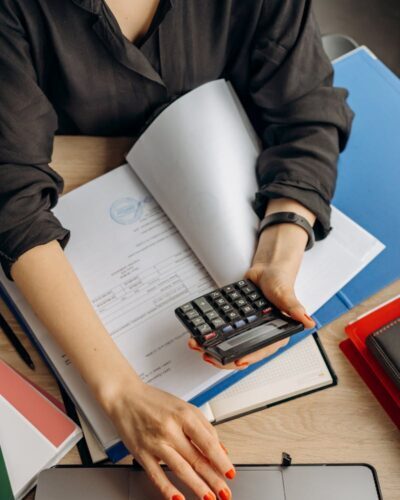 A business professional uses a calculator among documents and laptop on a desk for financial tasks.